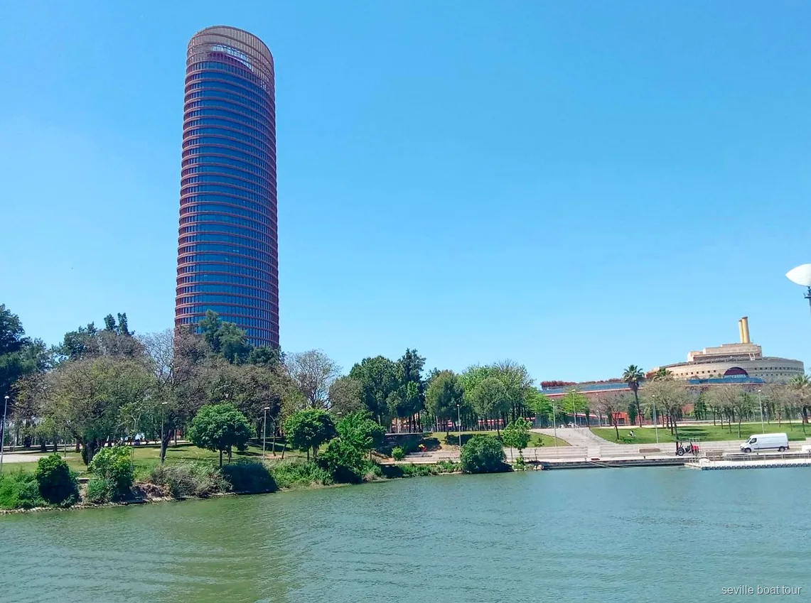 Torre Sevilla and the green Cartuja riverbank seen from a Seville boat tour on the Guadalquivir