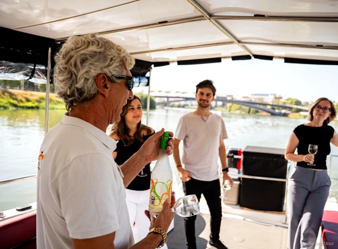 Host serving wine to guests under the shaded deck of a Seville boat tour on the Guadalquivir
