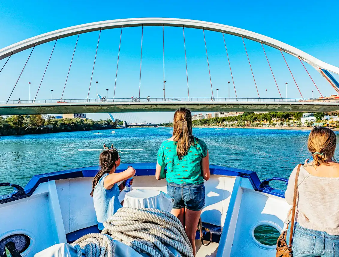 Pasajeros en la proa durante un paseo en barco por Sevilla acercándose al puente de la Barqueta