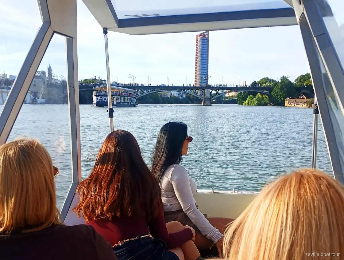 Pasajeras bajo el toldo del paseo en barco privado por Sevilla rumbo al puente de Triana y Torre Sevilla